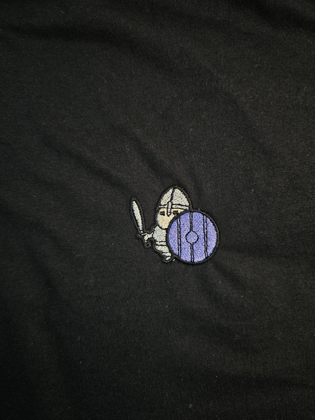 Detailed shot of an embroidered warrior holding their sword and shield up, ready to defend.