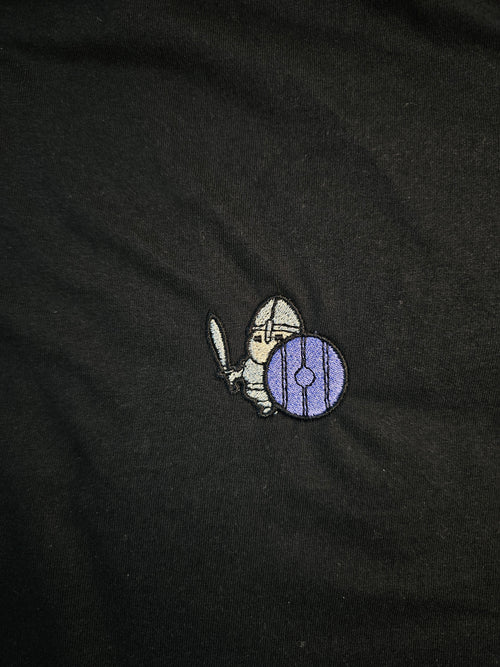 Detailed shot of an embroidered warrior holding their sword and shield up, ready to defend.